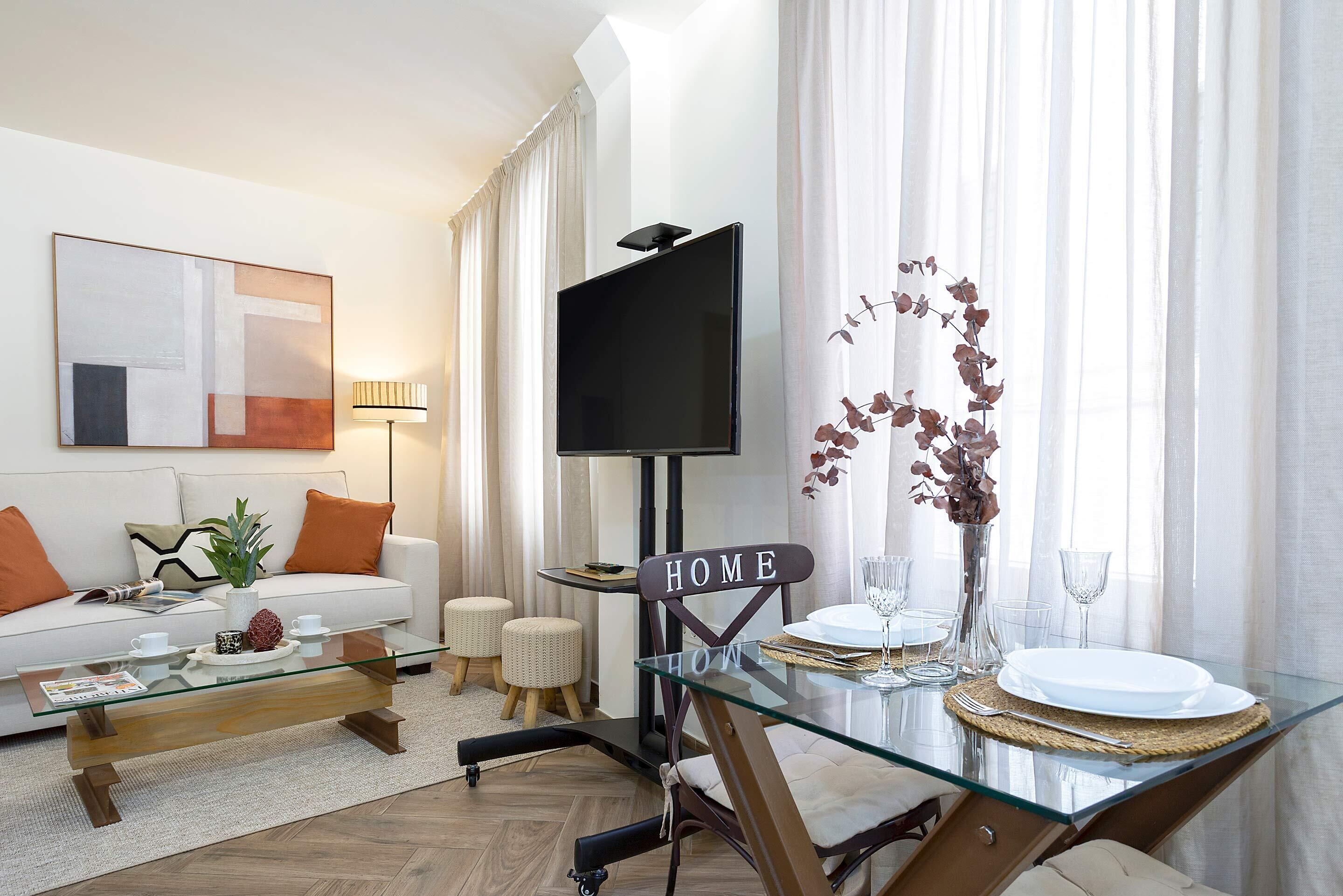 A modern living room with a glass coffee table, a sofa, a TV, and a dining area with a glass table and chairs.