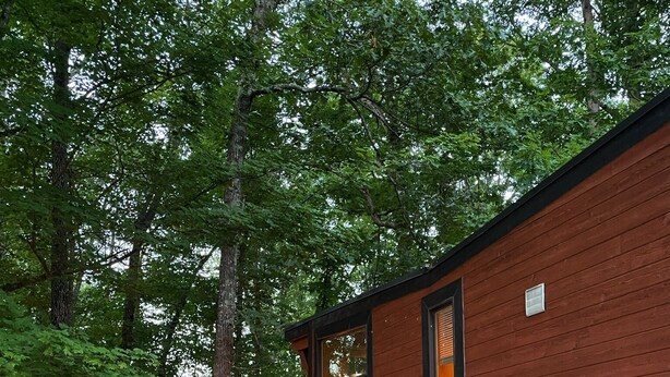A small, single-story cabin with a wooden exterior, a front door, and a window. It is surrounded by a gravel path and a bed of black mulch, with trees in the background. - Cozy cabin on Lookout Mountain (Lookout Mountain)