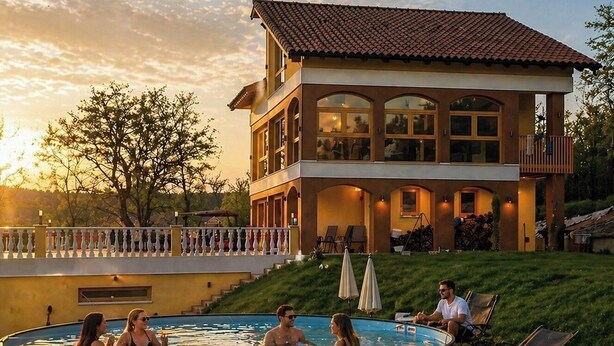 Una casa a due piani con piscina, area salotto esterna e un balcone.