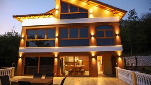 Una casa a due piani con un balcone, ampie finestre e una zona pranzo con sedie e tavolo.