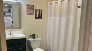 Un baño con inodoro blanco, lavamanos con espejo y cortina de ducha.