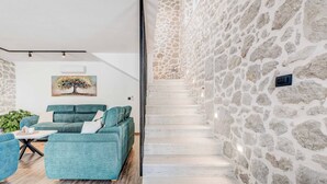 A modern living room with a stone wall, a staircase, and a sofa set.