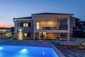 A modern two-story house with a swimming pool, stone facade, and a balcony with outdoor furniture. - Villa Elegant Stone (Runovići)