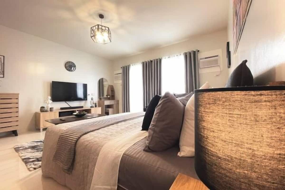 A modern hotel room with a bed, a television, a desk, and a window with curtains.