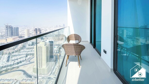 A balcony with a wicker chair, a glass railing, and a city view.