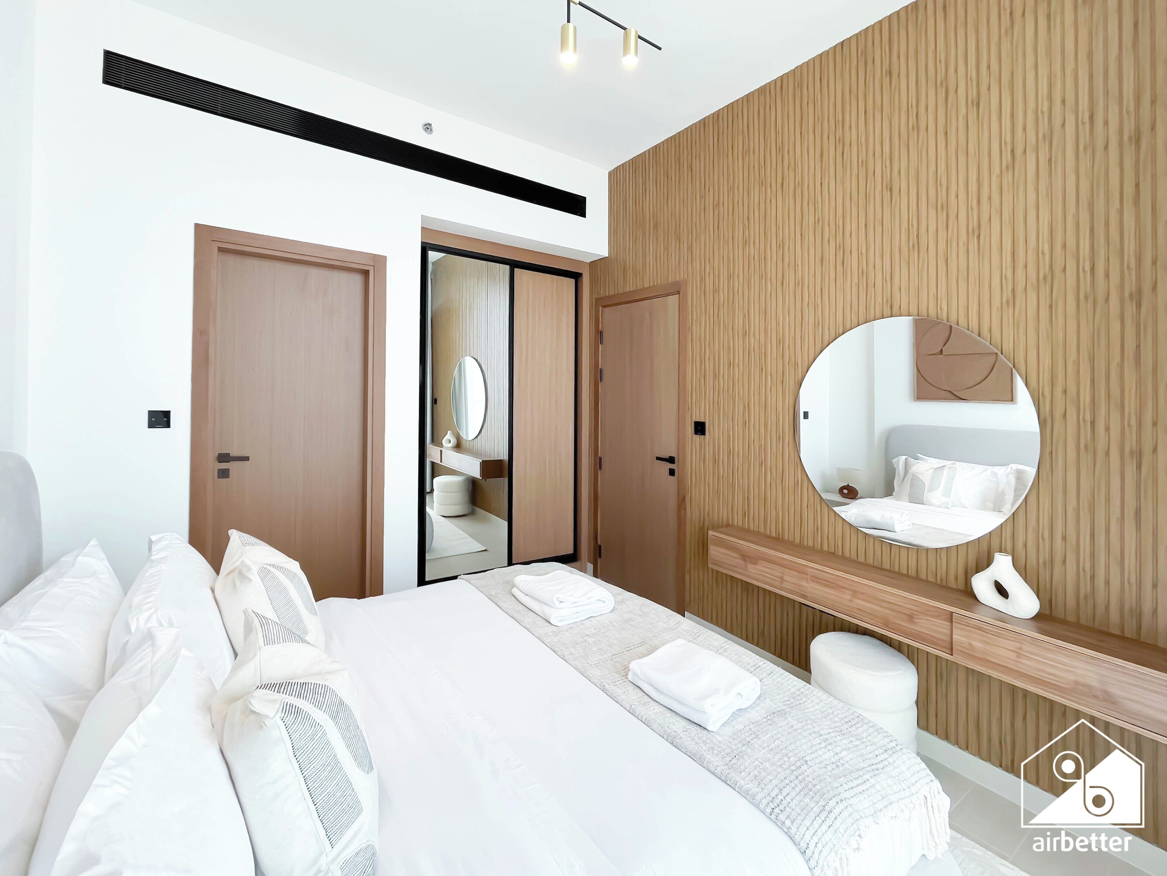 A modern hotel room with a large bed, a round mirror, wooden paneling, and a visible bathroom.