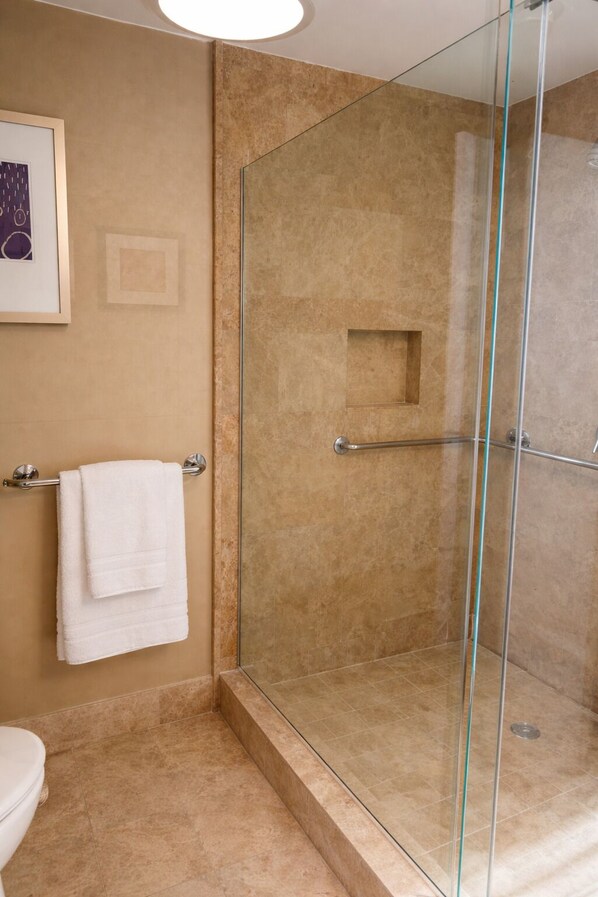 Une salle de bain avec une douche à parois de verre, une serviette blanche posée sur un porte-serviettes et un tableau encadré accroché au mur.
