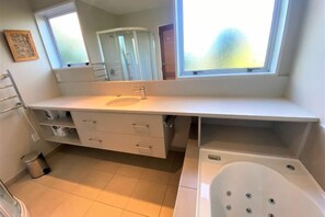 A modern bathroom with a large window, a bathtub, and a vanity with drawers. - Calm Swan Villa (Christchurch)