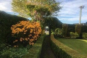 A pathway leading to a gated entrance surrounded by neatly trimmed hedges and a flowering tree. - Calm Swan Villa (Christchurch)