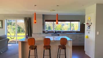 Una cocina moderna con una isla central, taburetes de bar, luces colgantes y vistas al exterior.