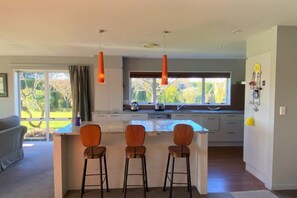 A modern kitchen with a central island, bar stools, pendant lights, and a view of the outdoors. - Calm Swan Villa (Christchurch)