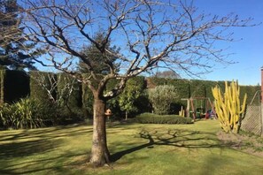 A garden with a large tree, neatly trimmed hedges, and a variety of plants. - Calm Swan Villa (Christchurch)