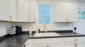 Una cocina moderna con armarios blancos, encimera negra y una ventana con persianas.
