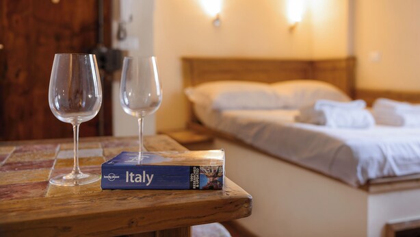 A wooden table with two empty wine glasses and a book titled 'Italy' in a hotel room.