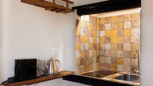A kitchen with a black countertop, a stainless steel sink, a coffee maker, and a kettle.