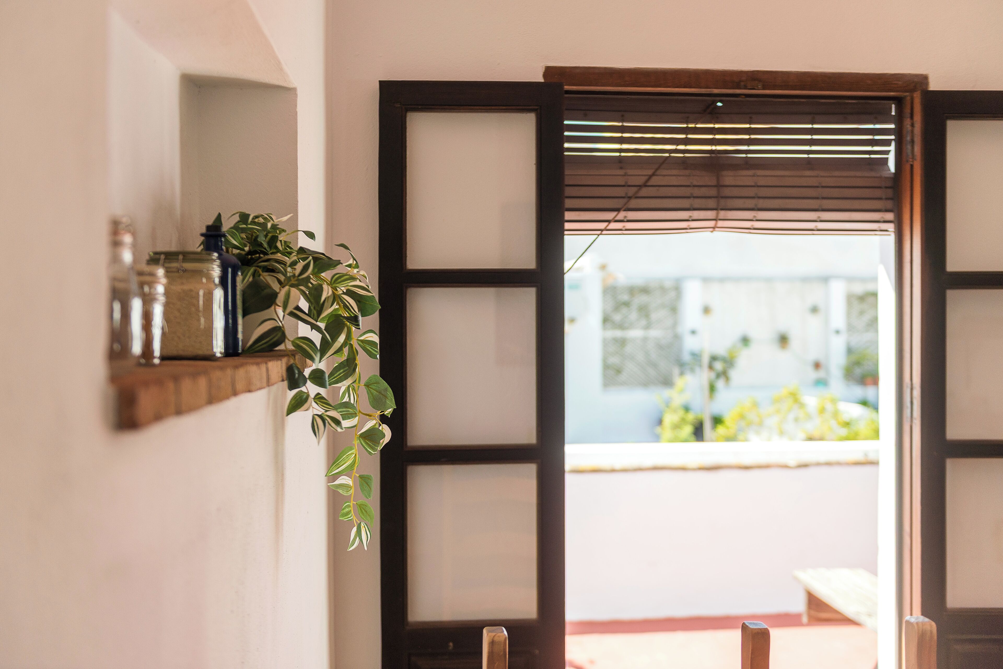 Una habitación con puerta corrediza, estante con frascos y una planta colgante.