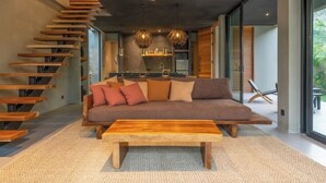 Een moderne woonkamer met een houten trap, een bank met kussens, een houten salontafel en hanglampen.