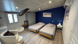 Ein Schlafzimmer mit zwei Betten, einem Sessel, einem Schreibtisch und einem Fenster.