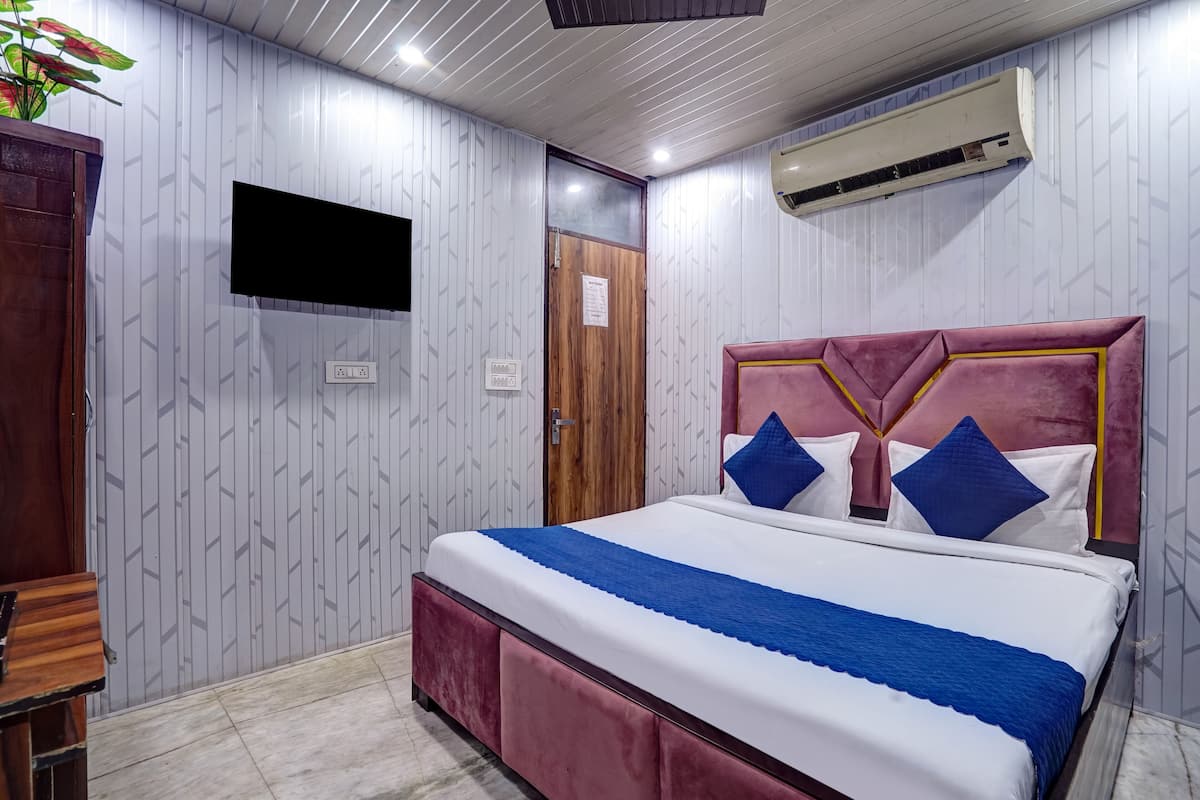 A bedroom with a large bed, a wooden wardrobe, a mounted TV, and an air conditioning unit.