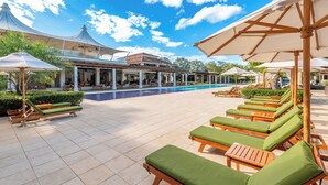 Zona junto a la piscina con sillones de descanso y sombrillas, piscina y área de estar cubierta.