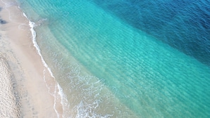 Vista aérea de una playa con agua turquesa cristalina y orilla arenosa.