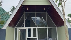 Un bâtiment moderne doté d’un toit en pente, de grandes fenêtres et d’un intérieur visible, comprenant un lit et un coin salon.