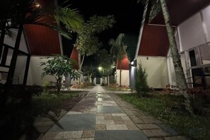 A pathway leading to a building with a red roof, surrounded by greenery and palm trees. - KALININGRAT COTTAGE 2 (Pronojiwo)