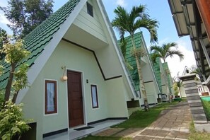 A row of modern, light-colored buildings with a green roof, a paved walkway, and palm trees. - KALININGRAT COTTAGE 2 (Pronojiwo)