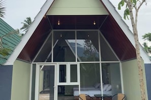 Una estructura moderna con techo triangular y entrada de vidrio que da a una cama y una mesa.