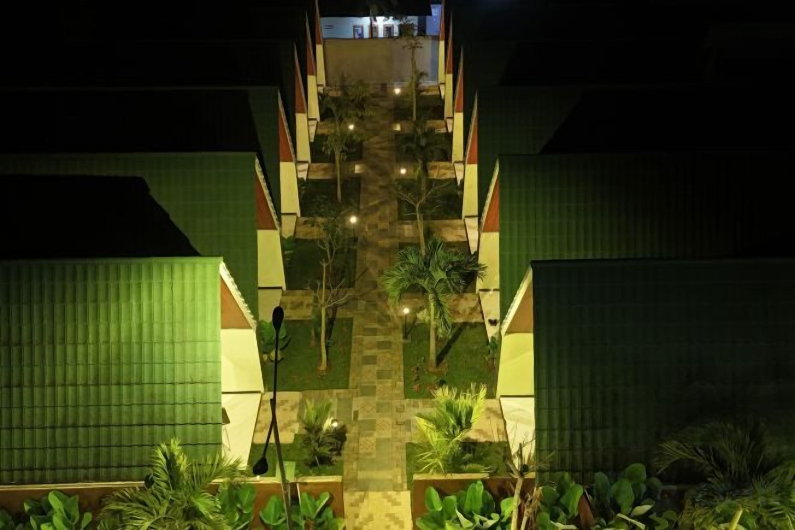 A nighttime view of a hotel entrance with a central staircase, surrounded by greenery and illuminated by pathway lights.