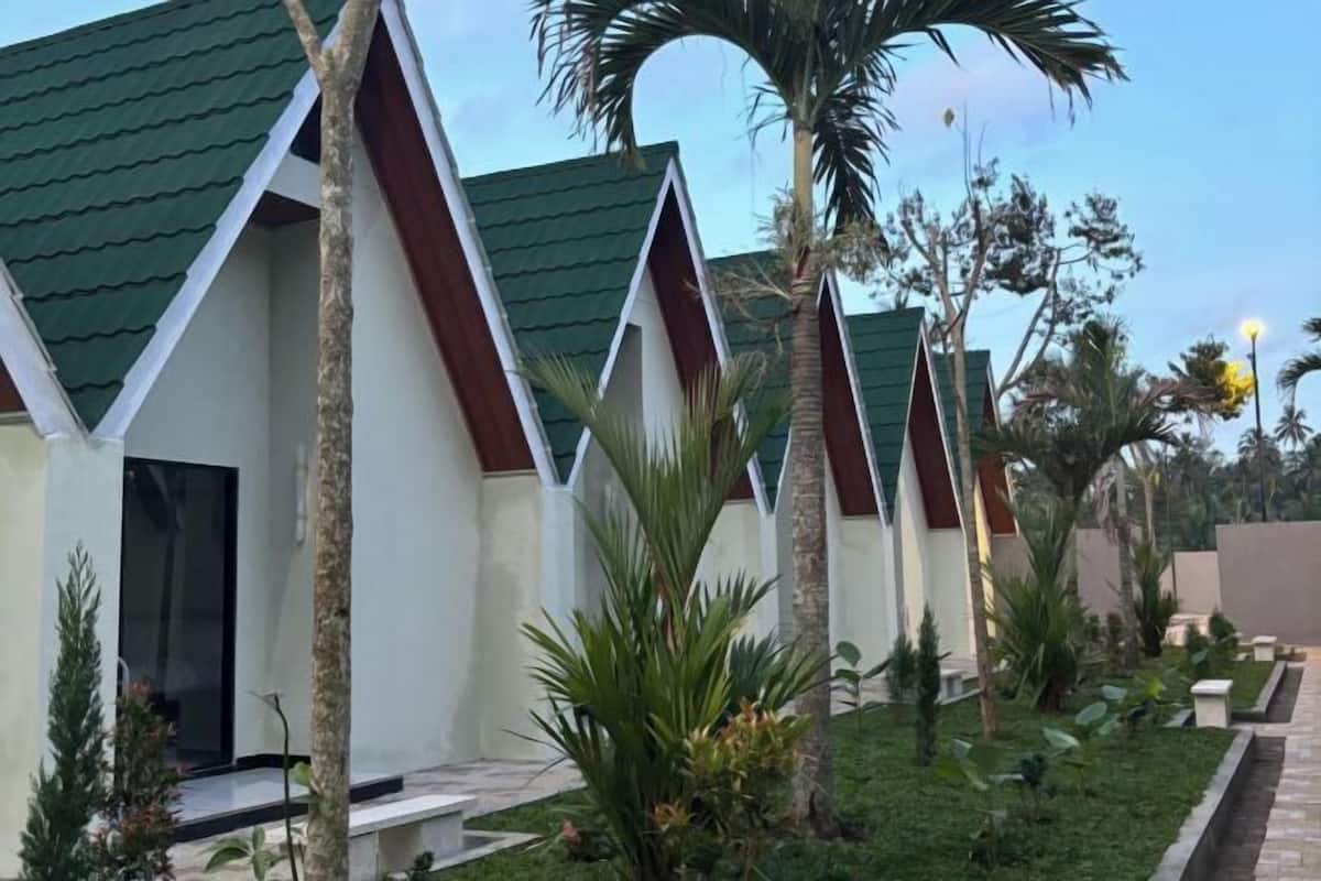A row of modern, triangular-roofed buildings with a well-maintained garden and palm trees.