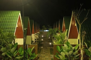 A pathway leading to a row of triangular-roofed structures, likely accommodations, with plants on either side. - KALININGRAT COTTAGE 2 (Pronojiwo)
