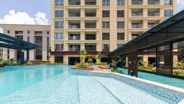A swimming pool with a tiled edge, surrounded by a building with multiple balconies and a covered walkway.