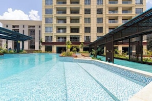 Ein Schwimmbecken mit Fliesenrand, umgeben von einem Gebäude mit mehreren Balkonen und einem überdachten Gang.