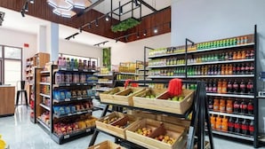 Interior de um supermercado com caixas de madeira cheias de frutas e legumes, prateleiras de bebidas e diversos produtos embalados.