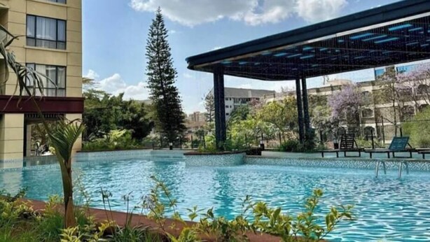 Piscina com pergolado e espreguiçadeiras, cercada por vegetação e uma árvore alta.