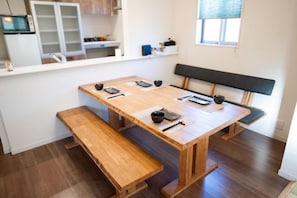 A wooden dining table with benches, a kitchen area with cabinets, and a window with blinds.
