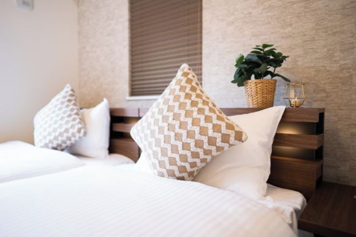 Ein Hotelzimmer mit einem Bett, zwei Kissen, einem Nachttisch, einer Pflanze und einer Kerze.