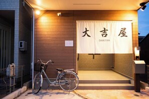 A building entrance with a bicycle parked outside, a sign with Japanese characters, and a tiled wall.
