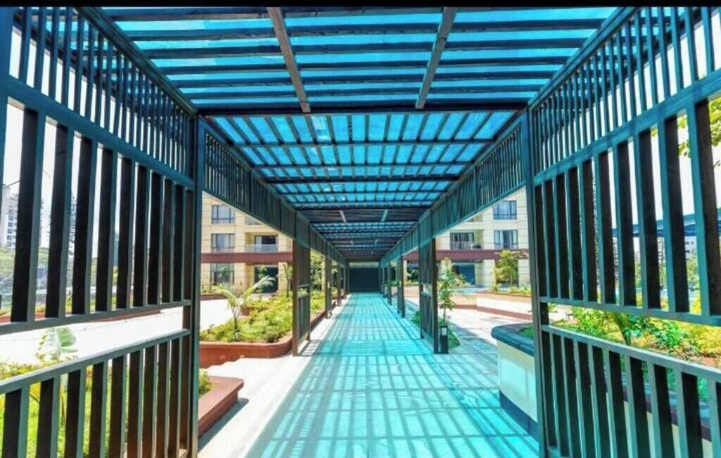 Un pasillo cubierto con barandillas de metal y paneles de vidrio, que conduce a un edificio con múltiples ventanas.