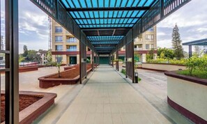 A covered walkway with a tiled floor, bordered by planters and a building with multiple floors. - 18th floor view apt with pool/gym/minimart at yaya (Nairobi)
