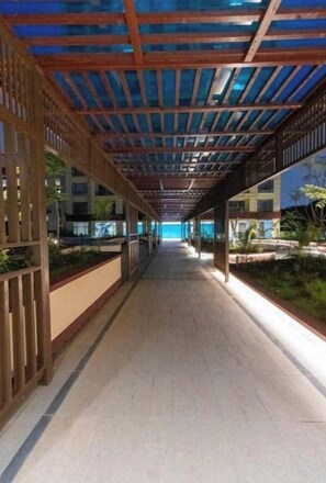 A corridor with a wooden ceiling and glass panels, leading to a pool area. - Luxe haven+ pool/gym/mini mart/king bed/coffeshop (Nairobi)