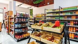 En dagligvarebutik med træfade fyldt med frugt og grøntsager, hylder med drikkevarer og et moderne interiør.