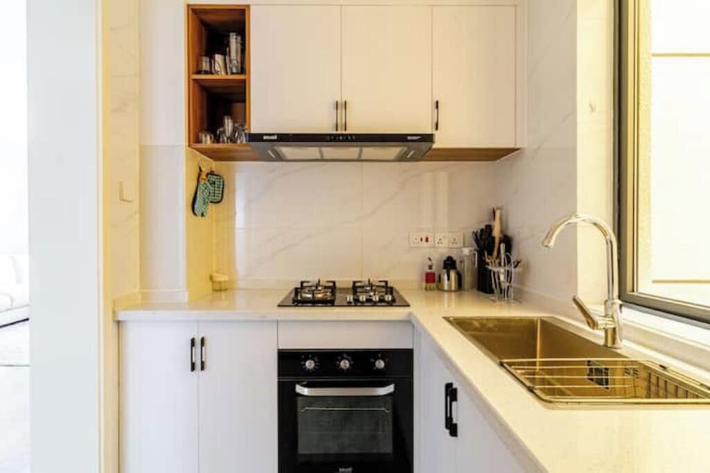 Een compacte keuken met witte kastjes, een gasfornuis, een oven en een roestvrijstalen spoelbak.