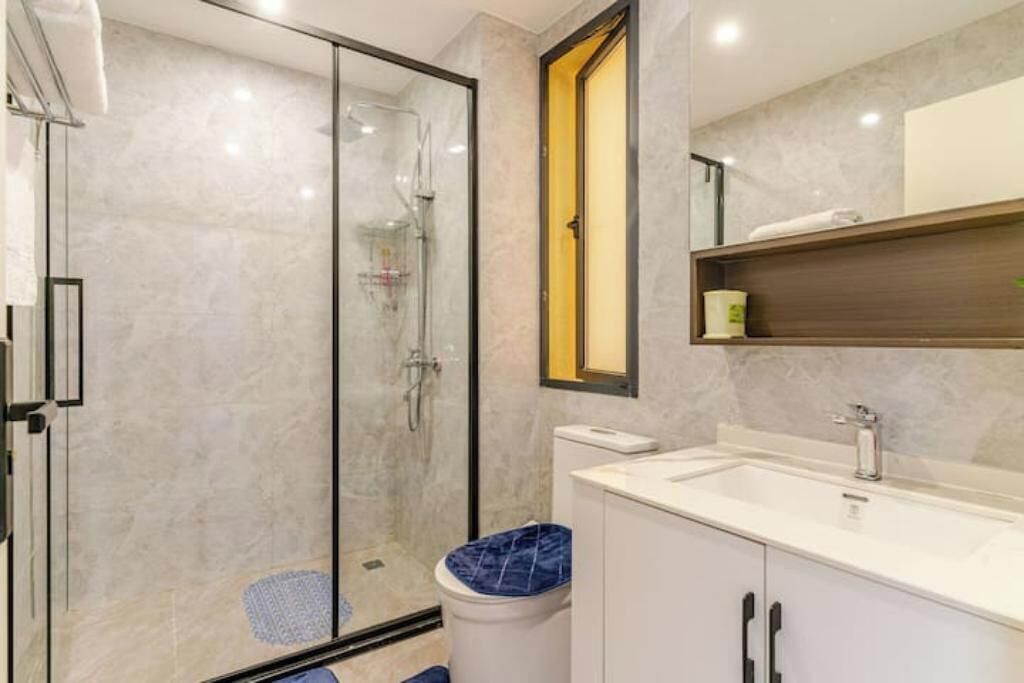 Une salle de bain moderne avec une douche à parois de verre, un lavabo blanc et des toilettes aux carreaux bleus.