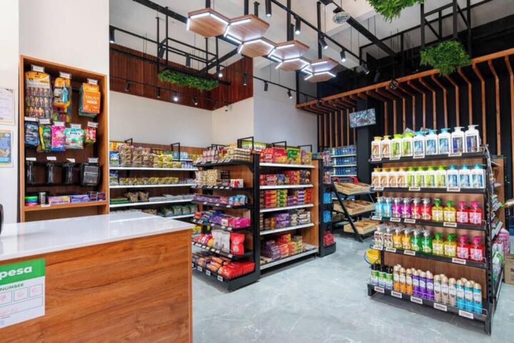 Een modern supermarktinrichting met houten schappen vol diverse producten, een kassa en een presentatie van flessen drank.