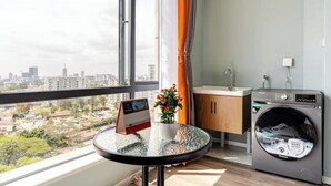 A room with a large window, a view of a cityscape, a small table with a plant, a sink, and a washing machine. - Deluxe Haven Kilimani with pool & gym yaya center (Nairobi)