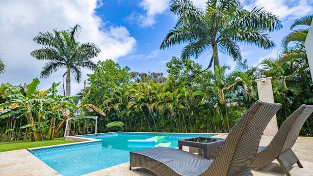 Un espace piscine doté de chaises longues, d’une piscine à l’eau d’un bleu cristallin et d’une végétation tropicale luxuriante.