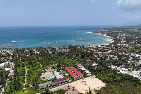 An aerial view of a coastal town with a beach, dense greenery, and residential buildings.