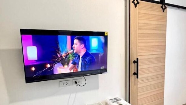 A television mounted on a wall, a wooden wardrobe, and a small storage unit with towels.